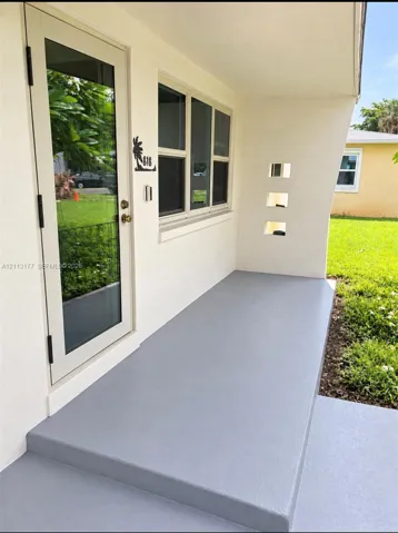 Covered entryway featuring a smooth concrete finish, custom cutout wall detailing, glass-panel entry door, and multi-pane windows