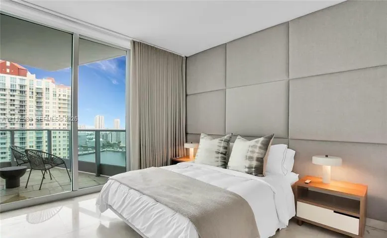 Floor-to-ceiling glass panel windows, expansive stone balcony with metal railing, and custom upholstered wall paneling