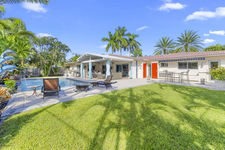 Backyard featuring a concrete pool deck, in-ground swimming pool, covered patio, manicured lawn, and mature palm trees