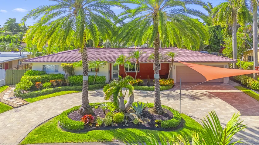 Single-story residence featuring a tile roof, paved circular driveway, mature palm trees, professional landscaping, and a two-car garage