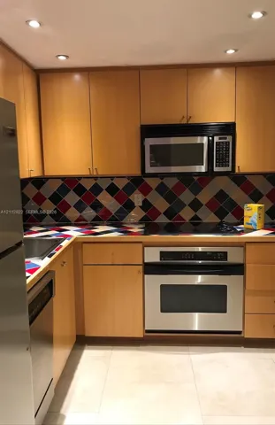 Kitchen featuring light wood-finish cabinetry, stainless steel appliances, multi-colored diamond-pattern backsplash, and recessed lighting