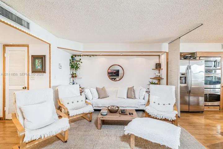 Open-concept interior featuring wood-finish flooring, recessed lighting, built-in shelving, a stainless steel double wall oven, and a stainless steel side-by-side refrigerator