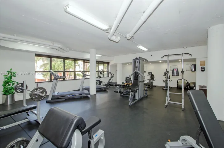 Fitness center featuring rubber flooring, expansive windows, exposed overhead infrastructure, and structural columns
