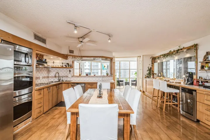 Kitchen featuring wood cabinetry, stainless steel double wall ovens, a dedicated wine refrigerator, track lighting, and wood-finish flooring