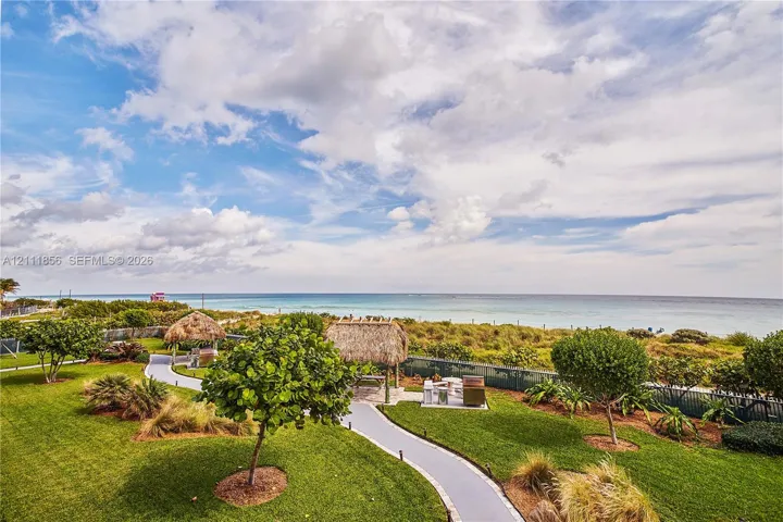 Coastal grounds featuring manicured lawns, mature landscaping, paved pathways, and multiple thatched-roof structures