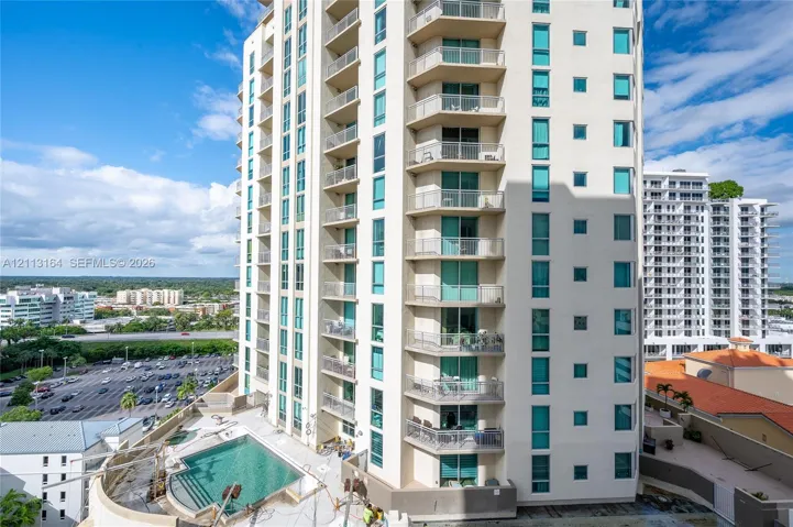 High-rise exterior featuring stacked private balconies, floor-to-ceiling glass windows, and a ground-level swimming pool with masonry decking
