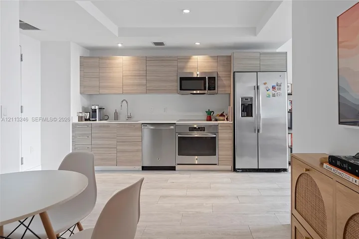 Kitchen featuring light wood-finish cabinetry, stainless steel appliances, a recessed tray ceiling, and stone-finish tile flooring