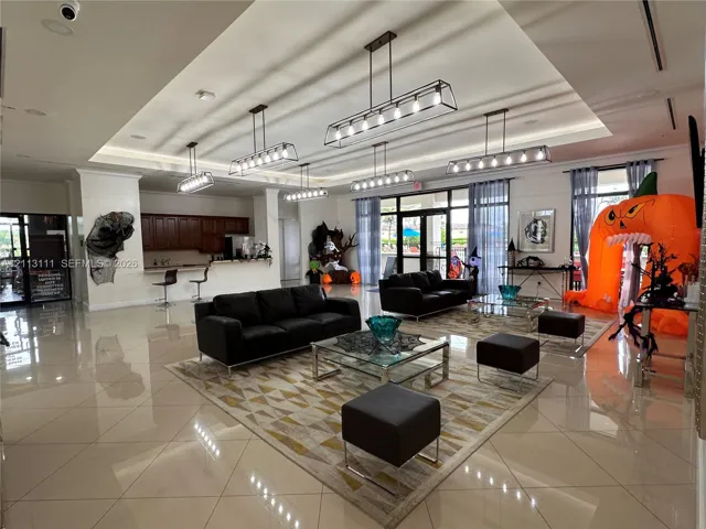 Open-concept room featuring large-format tile flooring, recessed tray ceiling, multiple rectangular linear chandeliers, and built-in cabinetry with a countertop bar