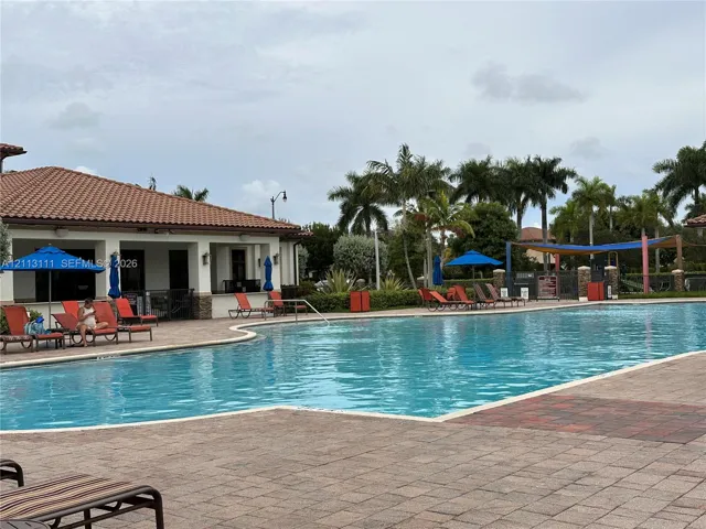 Community swimming pool featuring a paver deck, terracotta tile roof clubhouse, and mature palm landscaping