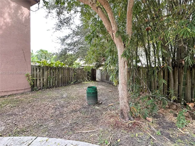 Side public yard featuring a wood privacy fence, mature trees, and natural ground cover