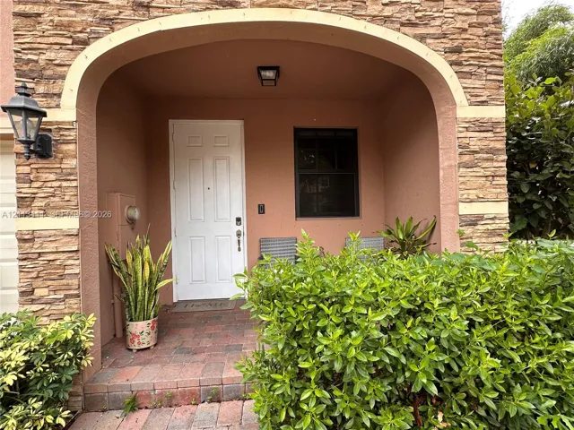 Covered entryway featuring a stacked stone facade, arched architectural detail, brick-paver flooring, and a six-panel door