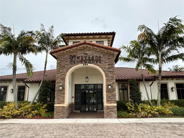 Clubhouse exterior featuring a stone-clad facade, arched entryway, terracotta tile roof, and brick-paver driveway