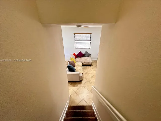 Staircase with a white-painted handrail, finished with wall-to-wall carpeting and square tile flooring