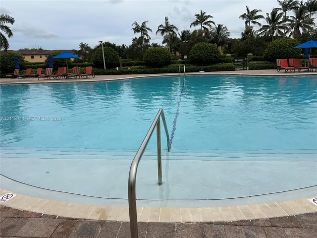 Swimming pool featuring a curved concrete deck, metal handrail, submerged entry steps, and paver stone hardscaping