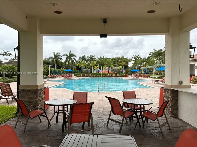 Covered outdoor patio with stone pillar accents, recessed lighting, and built-in serving counter, overlooking a paved pool deck and swimming pool