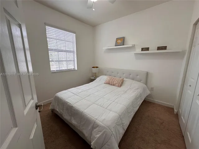 Neutral interior featuring wall-to-wall carpeting, window blinds, dual built-in wall shelves, and a bi-fold closet door