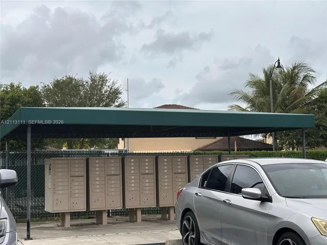 Covered communal mailbox station featuring a dark green metal awning, concrete base, and multi-unit locking mailboxes