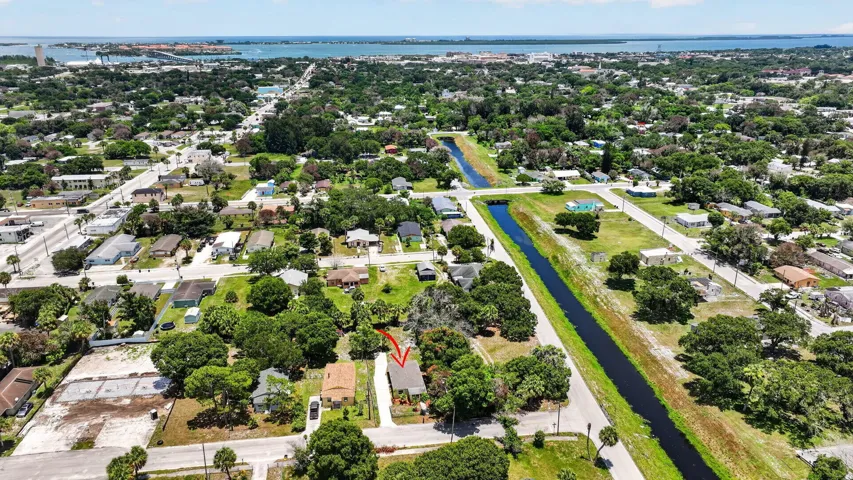 Aerial perspective featuring a single-story residence with a pitched shingle roof, paved driveway, and mature landscaping