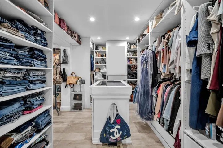 Walk-in closet featuring floor-to-ceiling white built-in shelving, a central storage island with a surface inlay, recessed lighting, and tile flooring