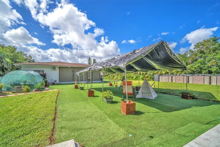 Expansive backyard featuring synthetic turf, a dome-style greenhouse, and a perimeter of mature trees