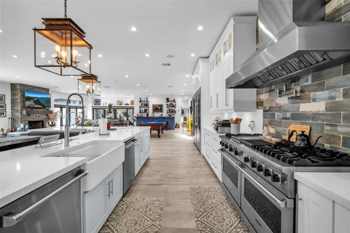 Kitchen featuring white cabinetry, quartz countertops, a farmhouse sink, stainless steel professional-style range with matching hood, and multi-tone subway tile backsplash