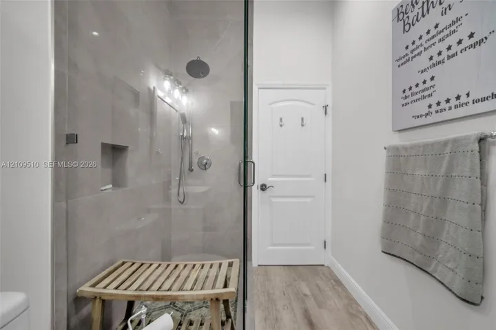 Walk-in shower featuring oversized tile walls, a recessed wall niche, a ceiling-mounted rainfall shower head, and a frameless glass door, complemented by wood-finish flooring