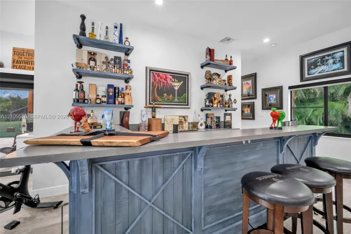 Custom built-in bar featuring a concrete countertop, plank-style wood cabinetry with cross-brace detailing, and industrial-style wall-mounted shelving