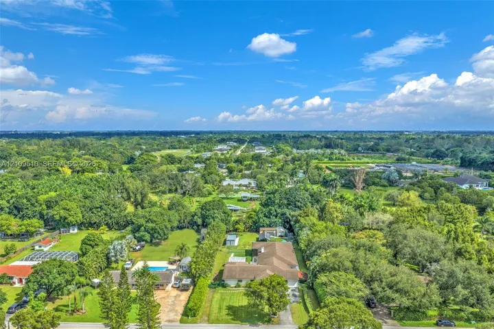 Aerial perspective of a sprawling property featuring extensive mature landscaping, a manicured lawn, and a multi-section roofline
