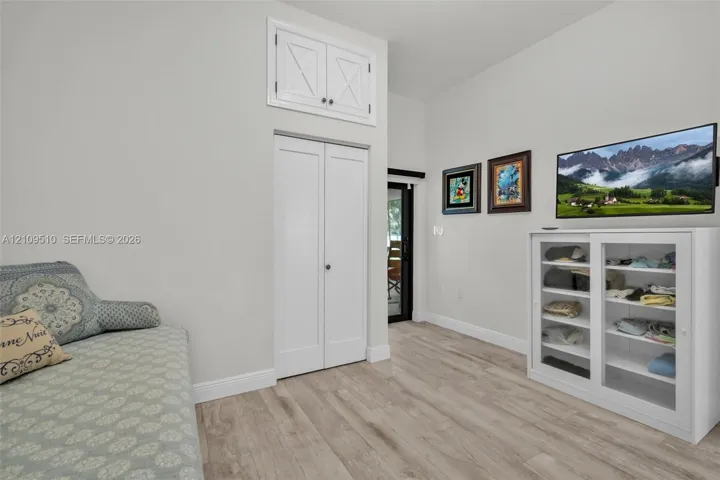 Wood-finish flooring, vaulted ceiling, dual-door closet, and upper storage cabinet with X-detail inlay
