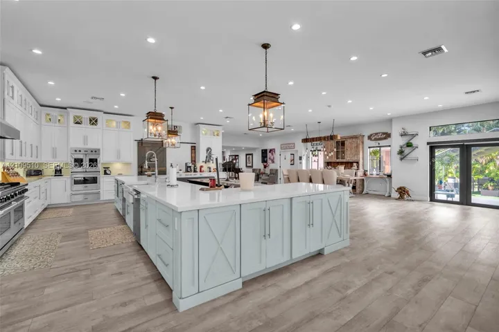 Open-concept kitchen featuring an expansive center island with stone countertops, white cabinetry, integrated stainless steel appliances, and wood-finish flooring throughout
