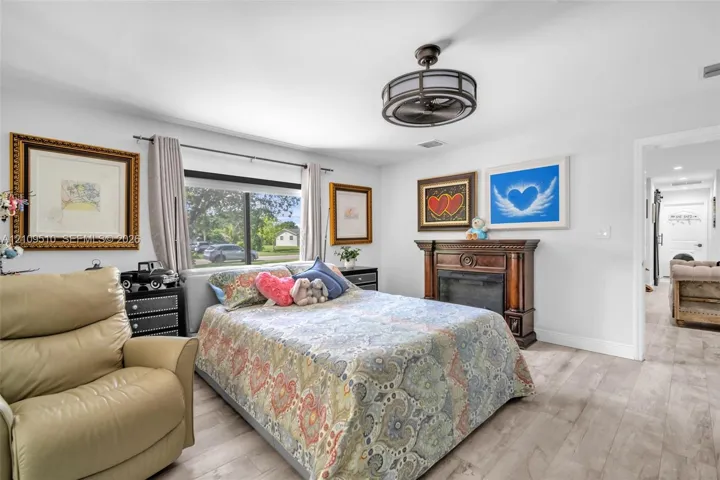 Wood-finish flooring, fireplace with a decorative wooden mantel, and a multi-blade ceiling fan with a circular cage housing