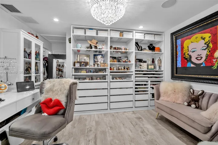 Custom built-in white cabinetry featuring extensive shelving, drawer storage, and glass-front display sections, complemented by wood-finish flooring and a crystal chandelier