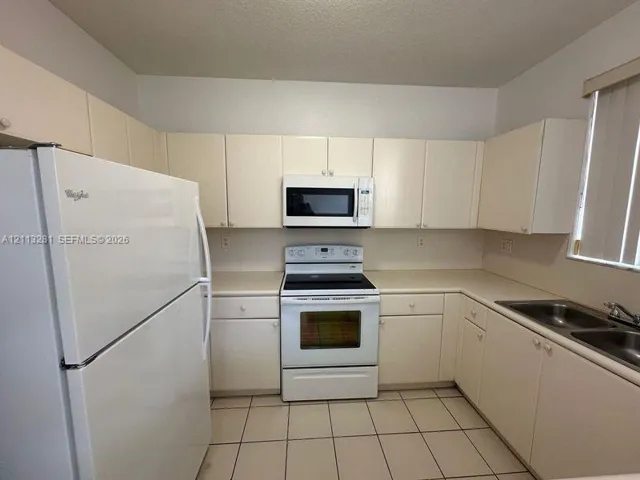 Kitchen featuring off-white cabinetry, solid-surface countertops, tile flooring, and a white appliance suite including a built-in microwave and range