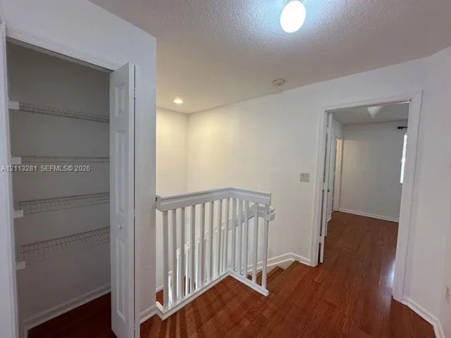 Hallway featuring wood-finish flooring, white picket-style stair railing, and a built-in closet with wire shelving