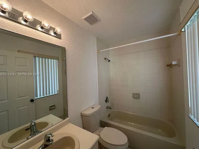 Bathroom featuring a vanity with an integrated sink, wall-mounted four-bulb lighting fixture, full-width mirror, and a tile-surround bathtub