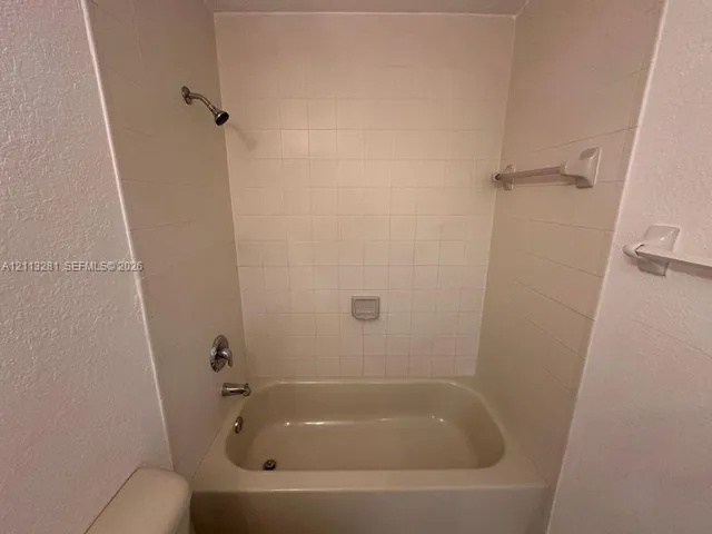 Bathtub surround featuring square ceramic tile, built-in soap dish, chrome shower head, and wall-mounted towel bars