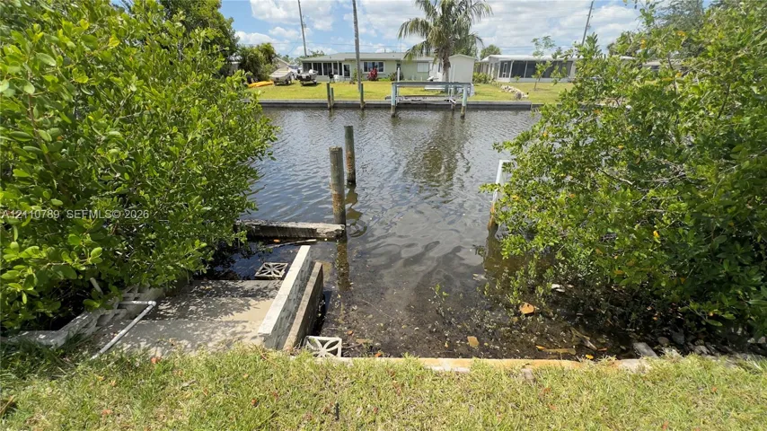 Canal-front property featuring a concrete bulkhead, private dock pilings, and stone stairs leading to the water