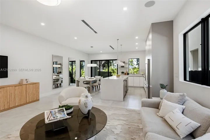 Open-concept living space featuring a central kitchen island with stone-finish waterfall countertop, large-format tile flooring, recessed ceiling lighting, and sliding glass doors