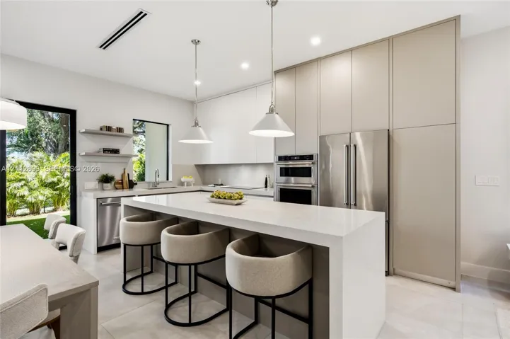 Contemporary kitchen featuring floor-to-ceiling flat-panel cabinetry, a waterfall-edge stone island, built-in stainless steel appliances, and dual pendant lighting