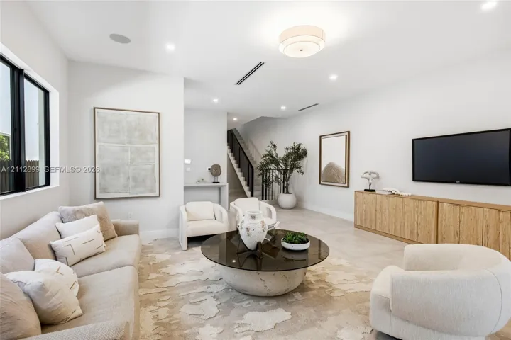 Open-concept living space featuring neutral oversized tile flooring, recessed ceiling lighting, a contemporary flush-mount fixture, black-framed windows, and built-in wood-finish cabinetry