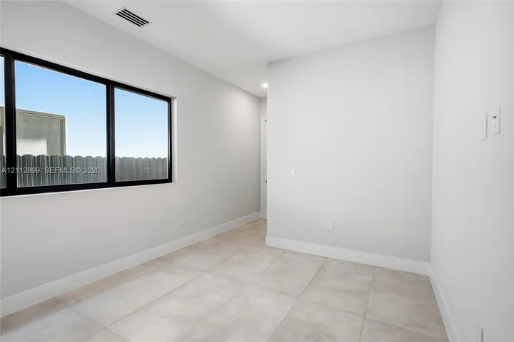 Neutral-toned tile flooring, oversized window with black frame, and smooth-finish walls