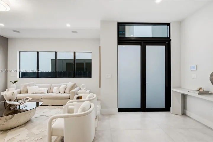 Double entry doors with frosted glass panels and an overhead transom window, large-format tile flooring, recessed lighting, and a built-in wall-mounted console