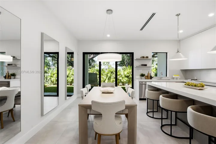 Modern kitchen featuring flat-panel cabinetry, a quartz waterfall island, large-format tile flooring, integrated linear lighting, and floor-to-ceiling glass sliding doors