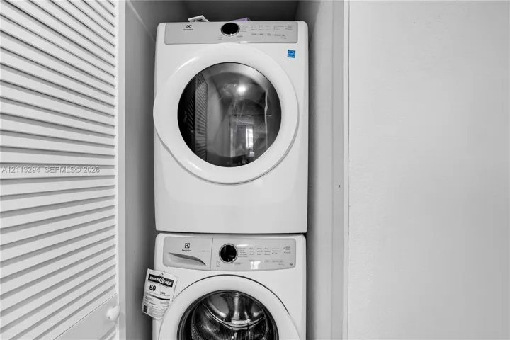 Stackable white front-load washer and dryer unit enclosed within a louvered-door closet