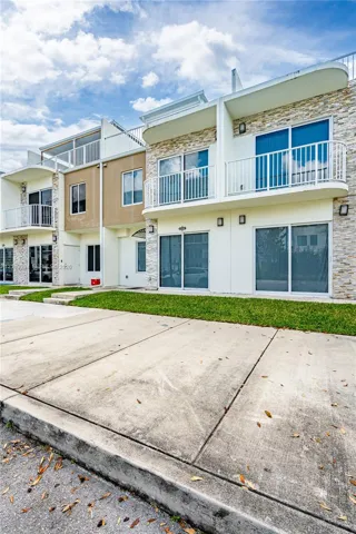 Multi-level exterior featuring stacked stone accents, smooth-finish siding, private balconies with white railings, and sliding glass doors