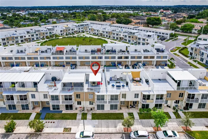 Aerial perspective of a multi-level residential complex featuring tiered roof terraces, white metal railings, stone veneer accents, and paved parking areas
