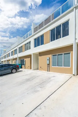 Contemporary multi-story exterior featuring a concrete driveway, smooth stucco finish, oversized windows, and a railed rooftop terrace