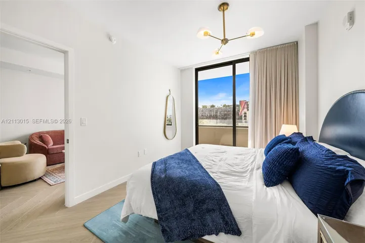 Bedroom featuring wood-finish flooring in a herringbone pattern, floor-to-ceiling glass sliding doors, a gold-toned multi-arm light fixture, and a balcony