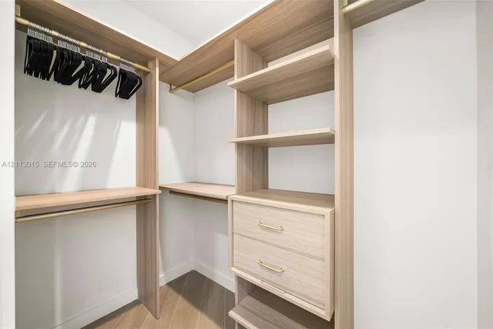 Custom reach-in closet featuring wood-finish cabinetry, built-in shelving, double drawers with gold-tone hardware, and integrated brass-finish garment rods