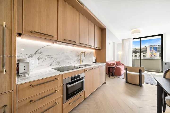 Kitchen featuring light-tone wood cabinetry, stone-patterned backsplash, built-in cooktop, stainless steel oven, and wood-finish flooring in a herringbone pattern